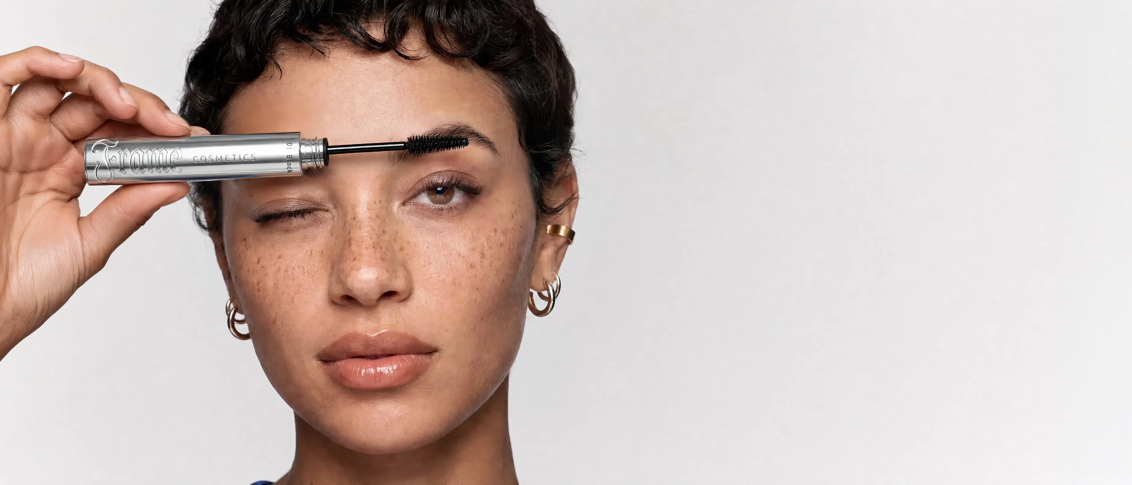 Beauty campaign still — model holding a mascara, generated on-brand